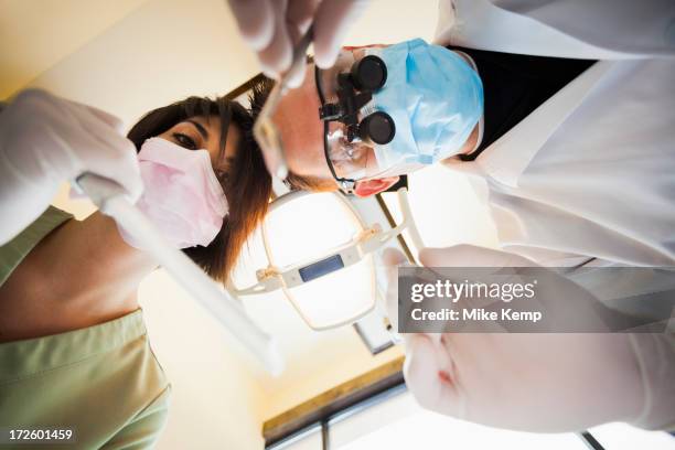 dentist and nurse towering over patient in office - surgical loupes stock pictures, royalty-free photos & images