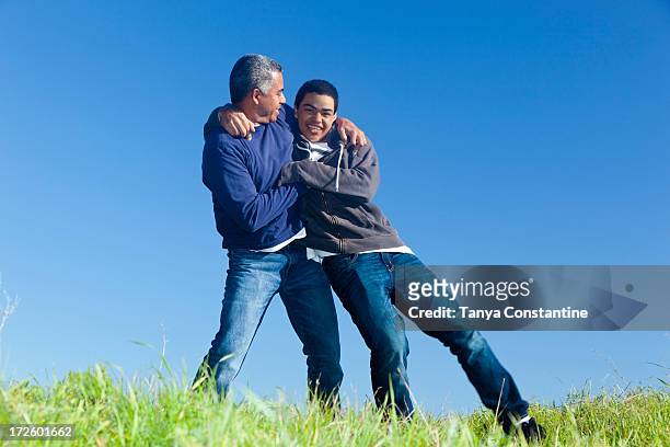 hispanic father and son playing in park - play fight stock pictures, royalty-free photos & images