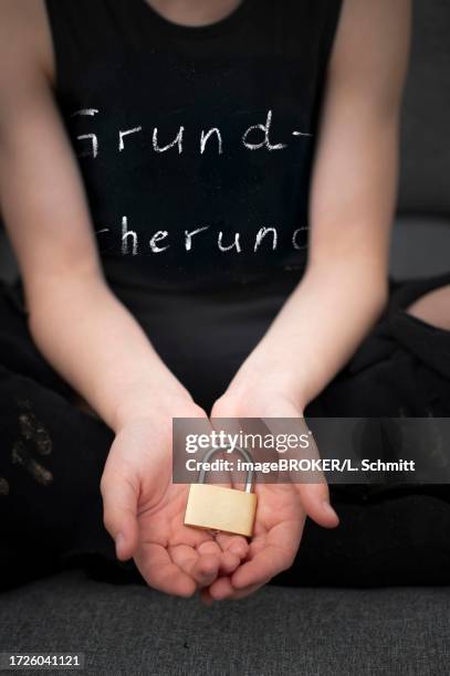 symbolic image of basic child security, child poverty, child in torn and dirty clothes symbolically holding a safety lock in his hands, state support, germany - 政府閉鎖 個照片及圖片檔