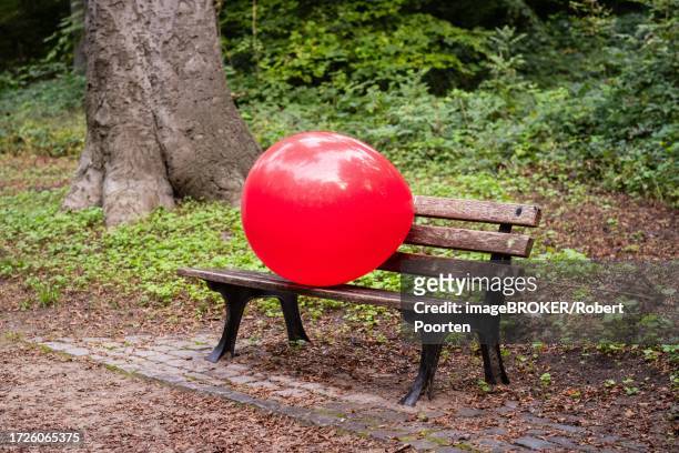 a red giant balloon on a bench in a park in duesseldorf, germany - empty bench with ballon stock pictures, royalty-free photos & images