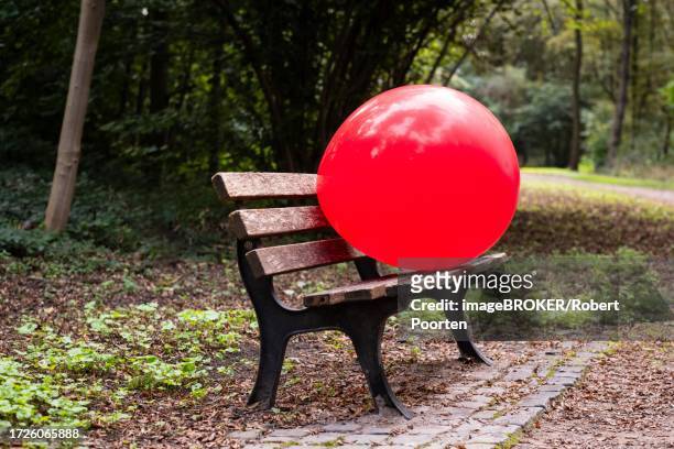a red giant balloon on a bench in a park in duesseldorf, germany - empty bench with ballon stock-fotos und bilder