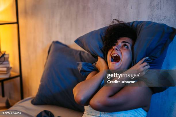 frustrated woman covering her ears with a pillow in her bedroom at night - waking up stock pictures, royalty-free photos & images