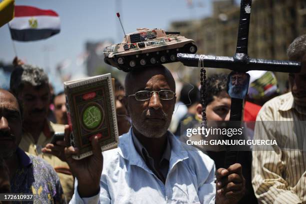 An Egyptian man, bearing a toy tank on his head, holds a cross and a copy of the Koran, Islam's holy book, as people gather in Cairo's landmark...