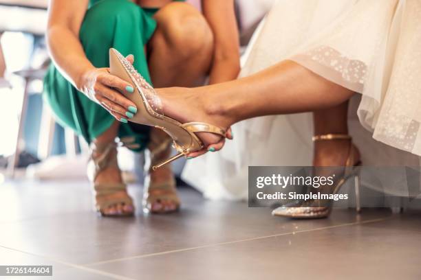 the maid of honor helps the bride to put on her shoes before the wedding ceremony. - wedding role stock pictures, royalty-free photos & images