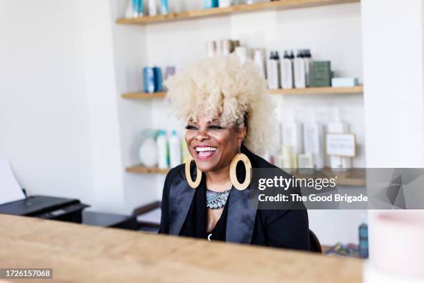 cheerful mature female receptionist sitting at desk in hair salon - salon reception stock-fotos und bilder