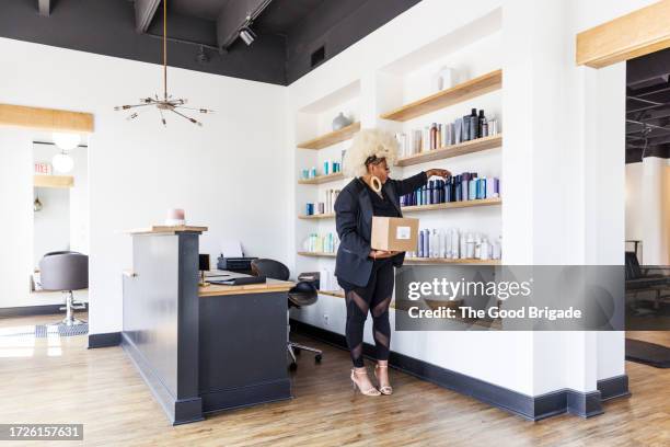 receptionist arranging merchandise on shelf at hair salon - salon reception stock-fotos und bilder