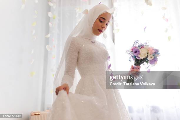 young muslim bride gently holds delicate fabric of wedding dress contemplating journey ahead - bride veil stock pictures, royalty-free photos & images