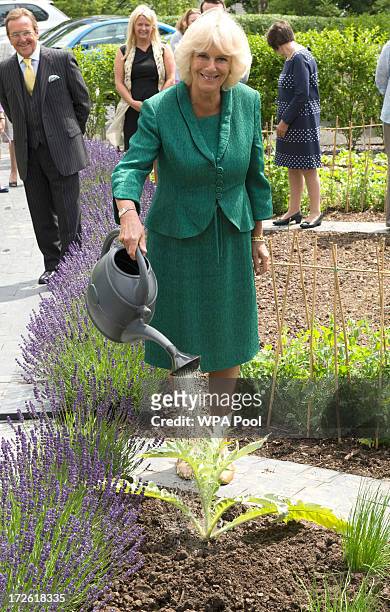 Camilla, Duchess of Cornwall waters an artichoke plant after planting it in the garden during her visit to Maggie's Cancer Caring Centre at Singleton...