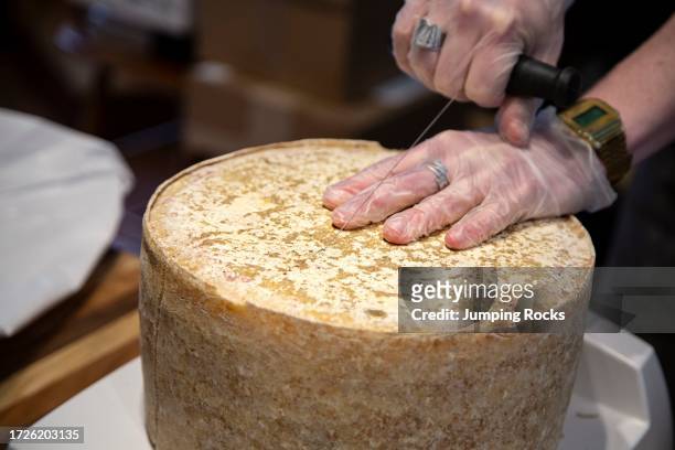 Cheese monger cutting wheel of 7 month aged Cloth Bound Cheddar, Grafton Village Cheese Shop, Grafton, Vermont, USA.
