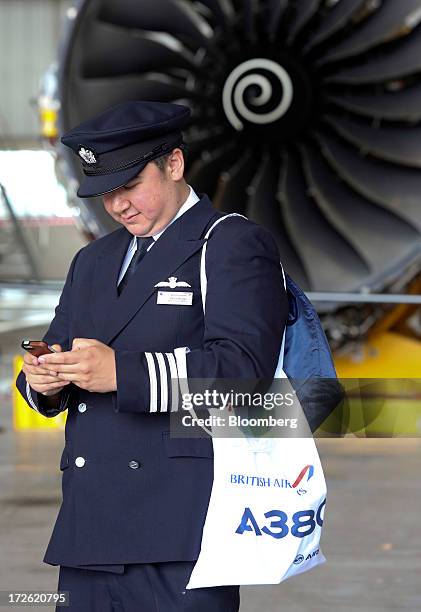 British Airways pilot carries an A380 branded bag as he uses a mobile device near an aircraft engine in the company's hangar at Heathrow airport in...