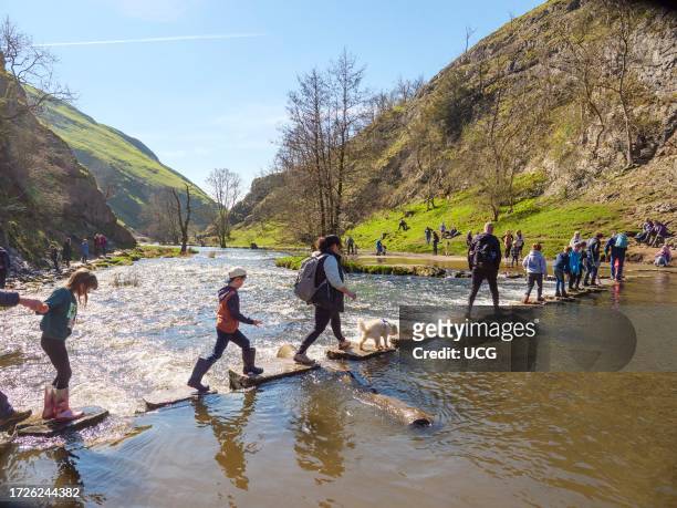 People crossing Stepping Stones over the River Dove in the Peak District, England, UK.