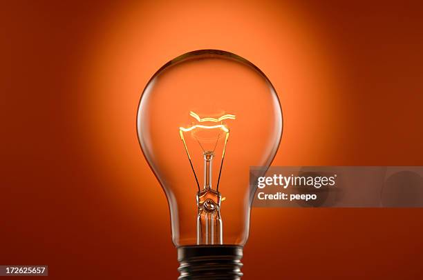 glowing lightbulb on orange background - orange object stock pictures, royalty-free photos & images