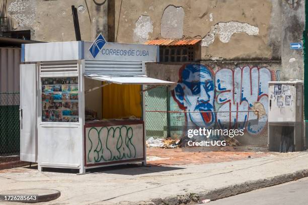 Havana, Cuba, A press kiosk belonging to Correos de Cuba. A garbage dump in the background by a dirty wall with graffiti.