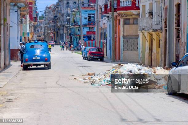 Havana, Cuba, Garbage dump on city street. A modern car and an vintage vehicles are parked in the residential district.