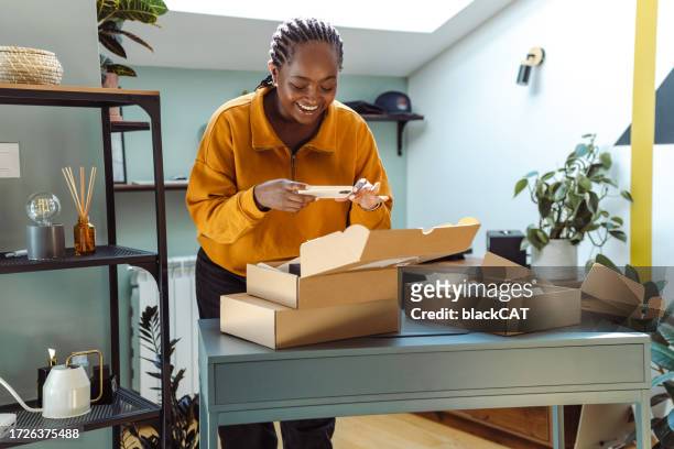 young african-american holding cardboard boxes and using smart phone - return merchandise stock pictures, royalty-free photos & images
