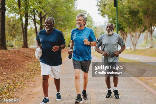 drei ältere freunde laufen zusammen in einem öffentlichen park - 3 old men jogging stock-fotos und bilder
