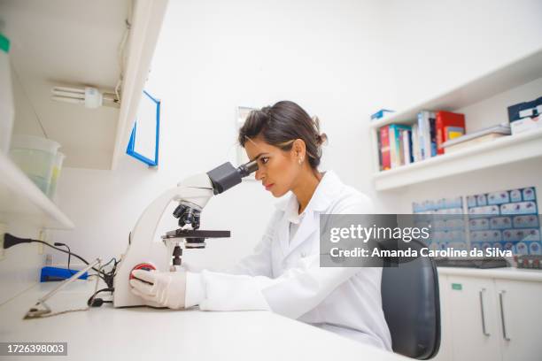 brazilian woman works in a medical laboratory, sitting in front of a microscope - electron microscope stock pictures, royalty-free photos & images