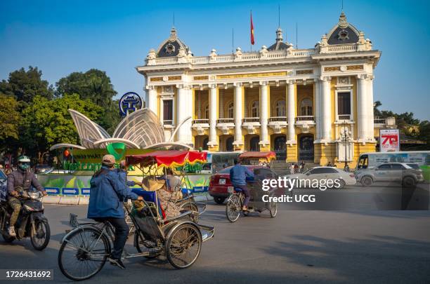 Cyclos carrying tourists and other traffic passes in front of the French colonial-era Hanoi Opera House, or Nha Hat Lon, in Hanoi, Vietnam.