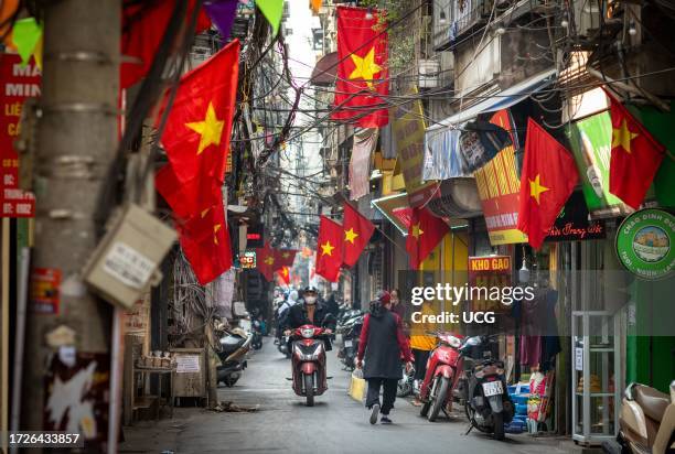 People go about daily life under Vietnamese flags in a narrow residential alleyway called Kham Thien Market in Hanoi, Vietnam.