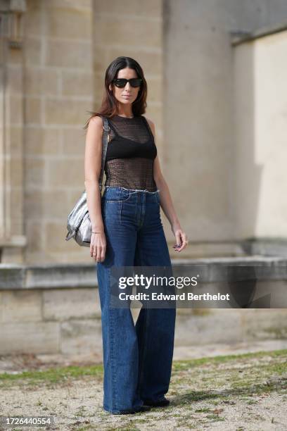Guest wears a balck mesh see-through tank top with printed logo monograms, black bras, blue denim jeans pants, outside Givenchy, during the...