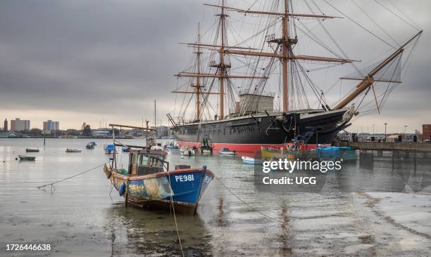 Small fishing boat called Mizpah III moored in Portsmouth Harbor in front of the famous warship HMS Warrior, the first ironclad naval ship in the...