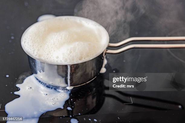 boiling milk is pouring out to the stove - traboccante foto e immagini stock