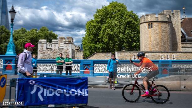 Cyclists participating in RideLondon 2022 takes a selfie on his mobile phone as he approaches the finish line on Tower Bridge in London. The event...