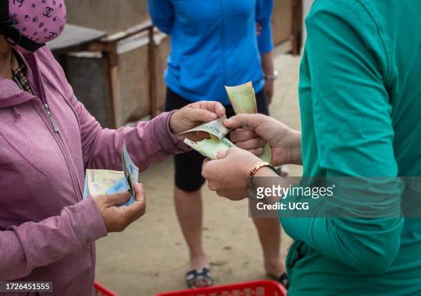 Two Vietnamese woman complete a cash transaction in the Vietnamese currency dong to buy fresh fish on My Khe beach in Danang, Vietnam.