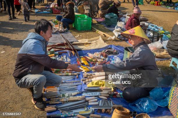 White Thai ethnic minority man buys a handmade knife at a knife stall in a busty open-air market in Mai Chau, Vietnam.