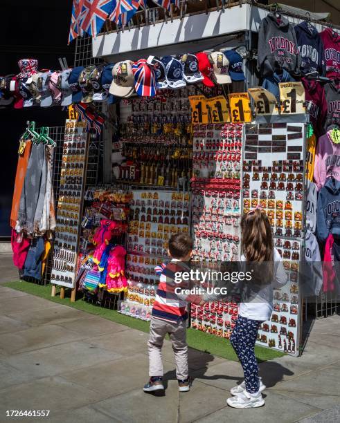 Brother and sister stop to look at tourist souvenirs at a stall on Oxford Street, London, UK.