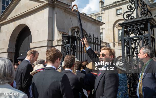 Man in a suit with a British Army Horse Guards regimental tie holds up an umbrella in a crowd of VIPS waiting to enter Horse Guards Parade for the...