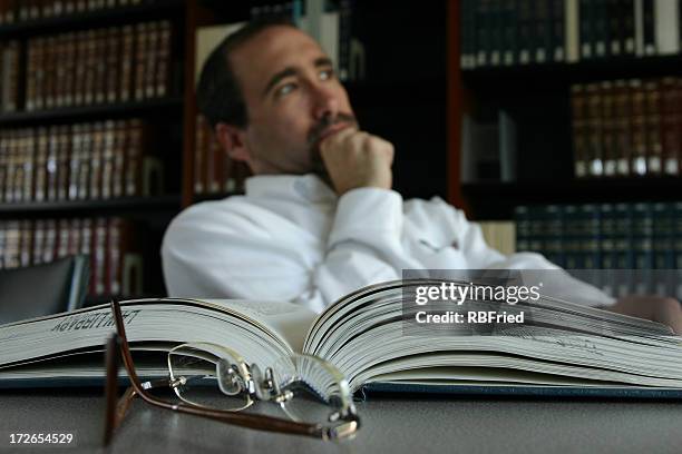 man thinking at his desk by an open book in a library - deep conversation stock pictures, royalty-free photos & images