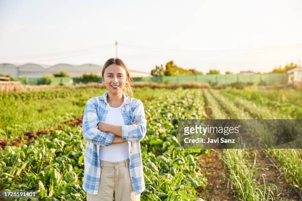 portrait of a young farmer working in the field of ecological vegetables looking at the camera with her arms crossed. - farmer arms crossed stock pictures, royalty-free photos & images