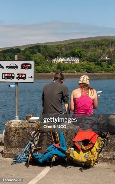 Portree, Isle of Skye, Scotland, UK, Couple of holidaymakers eating lunch while sitting on the harbor wall in Portree a coastal town and seaport,.