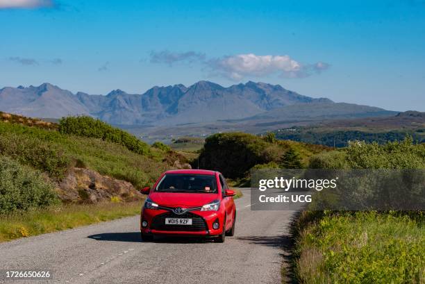 Isle of Skye, Scotland, UK, Small red car and scenic countryside view across to the Cuillin Hills with a blue sky. Isle of Skye, UK.