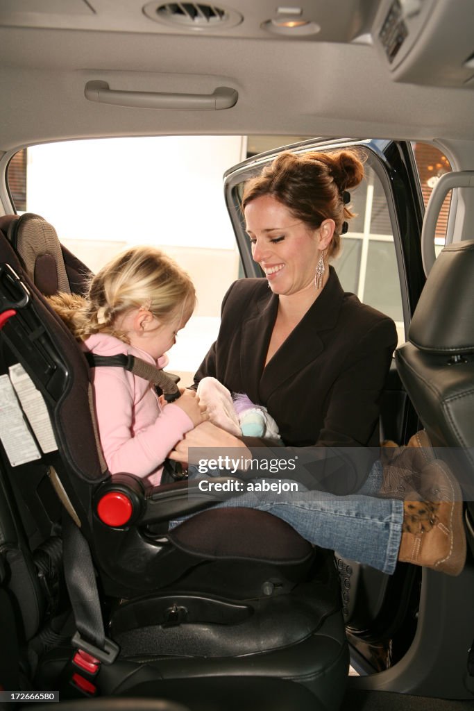 Smiling mother buckling her daughter into car toddler seat