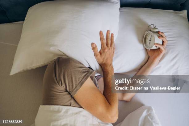 sleeping man disturbed by alarm clock early in the morning - alarm clock hand stock pictures, royalty-free photos & images