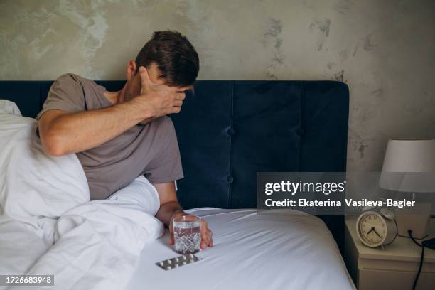 man in bed with headache drinking pills - the morning after stock pictures, royalty-free photos & images