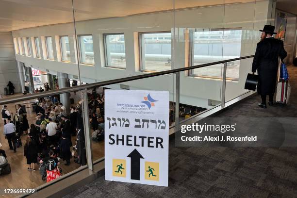 Shelter" sign is displayed as people arrive in Israel overlooking others waiting to board flights at Ben Gurion Airport on October 09, 2023 in Lod,...