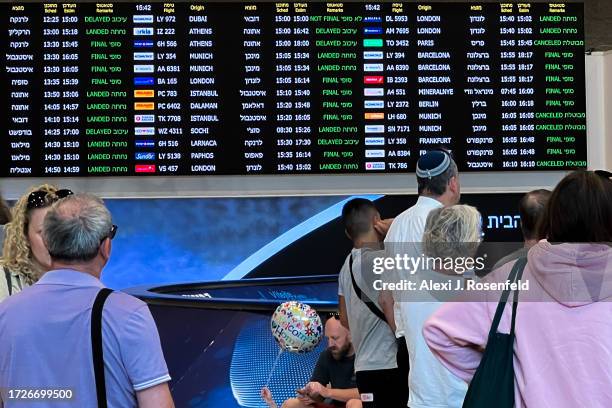 People wait for passengers arriving in near a sign showing landed and cancelled flights at the arrivals hall at Ben Gurion Airport on October 09,...
