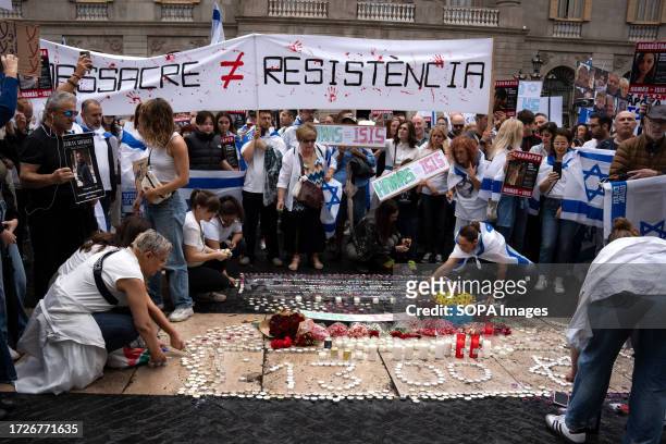 Protesters lay flowers and candles on the ground while holding placards during a demonstration by the Jewish community in Barcelona's Plaça Sant...