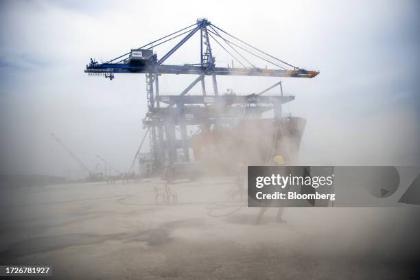 Workers in front of a gantry crane and the Zhen Hua 15 heavy load cargo carrier at the Vizhinjam transshipment container port, developed by Adani...