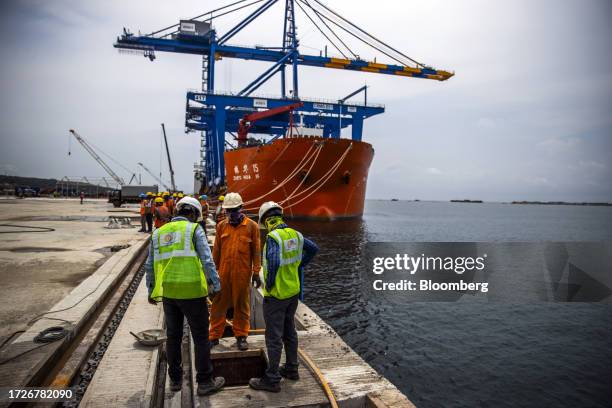 Workers in front of a gantry crane and the Zhen Hua 15 heavy load cargo carrier at the Vizhinjam transshipment container port, developed by Adani...