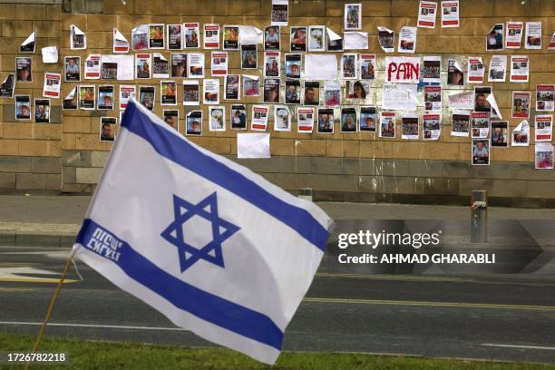 The Israeli flag is place close to a wall plastered with images of Israeli hostages snatched by the Palestinian militant group Hamas last week in a...