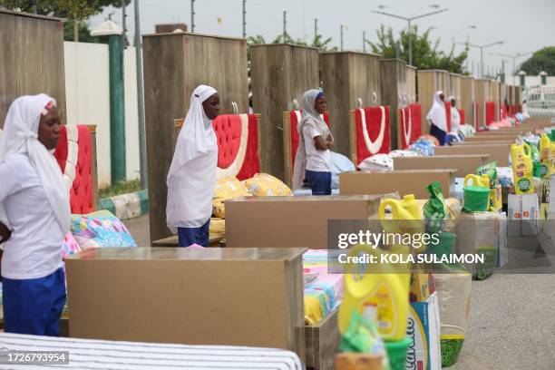 Household items given to couples are seen beside brides at the venue of a wedding reception at the Kano state governor's office after taking part in...