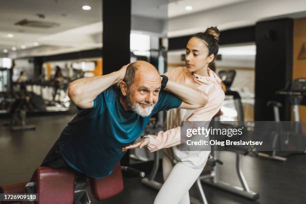 old man doing hyperextension exercise for strong back and young coach helping and supporting him - fitness instructor stock pictures, royalty-free photos & images