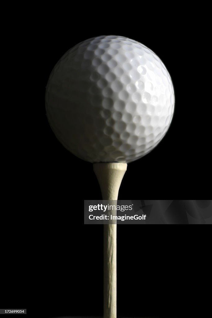 Dimly lit golf ball on a tee with half in shadow.