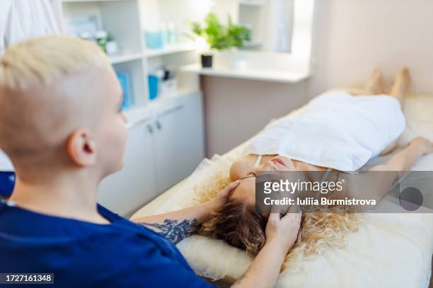 skilled female therapist with bold haircut administers myofascial massage to female client head - administers stock pictures, royalty-free photos & images
