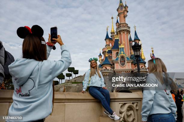 Visitors wearing emblematic Mickey and Minnie Mouse ears take selfies in front of the Sleeping-Beauty-inspired castle in Disneyland Park at...