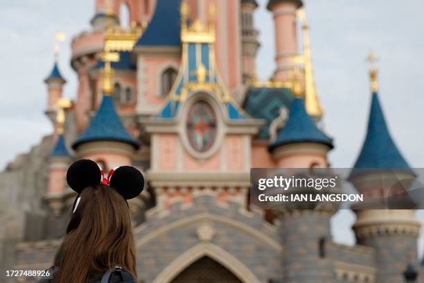 Visitors wearing emblematic Mickey and Minnie Mouse ears look on, in front of the Sleeping Beauty-inspired castle in Disneyland Park at Disneyland...